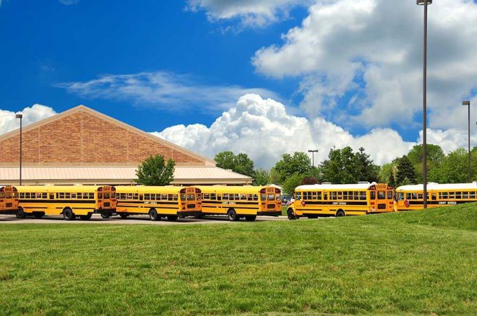 shutterstock_12885175 A row of yellow school buses parked in front of a school building under a cloudy sky