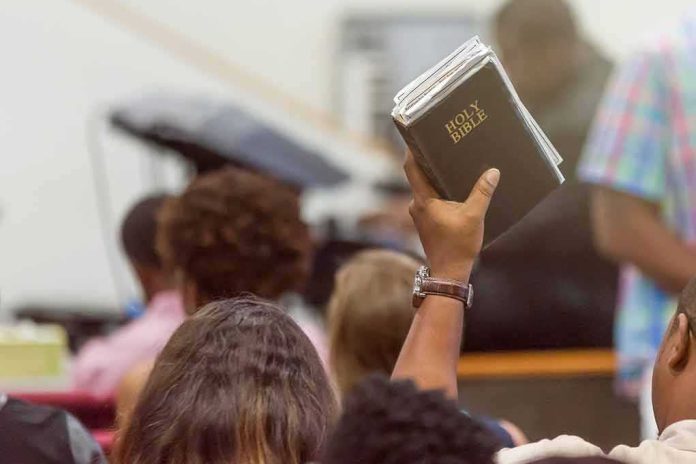 shutterstock_1294946557 Hand holding a Bible in a crowded church service