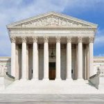 Justice Alito Steps Aside From Major Supreme Court Case Front view of the Supreme Court building with large columns and steps under a blue sky