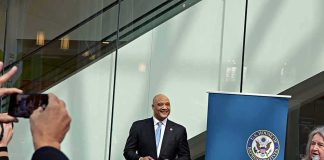 Man in a suit at a public event near a blue banner