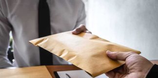 Hands exchanging a brown envelope across a desk