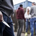 Ninja Sword Loophole Kills Teen Person holding a folding knife near a group of people in an alley