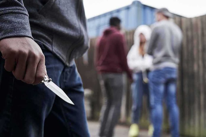 shutterstock_1433575952 Person holding a folding knife near a group of people in an alley