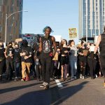 Peaceful Protest—Or Paid Blockade? Protesters march on a city street holding signs