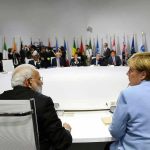 Angela Merkel and Narendra Modi seated at a large round table during an international summit