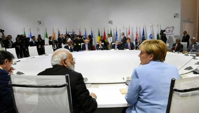 Angela Merkel and Narendra Modi seated at a large round table during an international summit