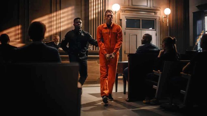 shutterstock_2056444856 Defendant in orange jumpsuit escorted by officer in courtroom