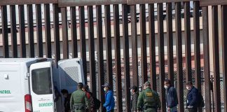 Trump REJECTS Report of ICE Pullback Border agents escort a group near a tall fence and a patrol van