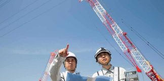 Two construction workers reviewing plans at a site with cranes