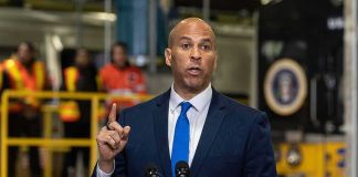 Senate Democrat Makes Explosive Midterm Election Claim Cory Booker speaks at a podium, with Caraun Reid in the background