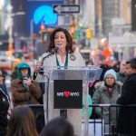 What Happens If Politicians Ignore SCOTUS? Kathy Hochul speaks at a clear podium in a city street; Josh Boyce stands among the crowd