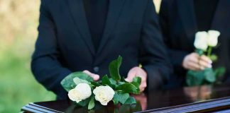 mourners place white roses on a wooden casket