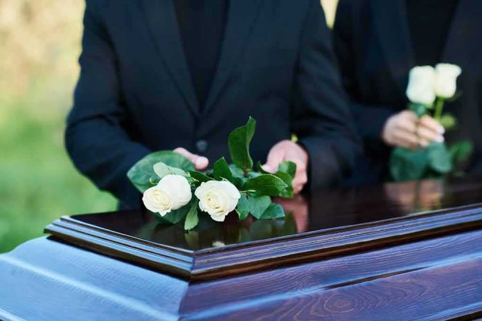 shutterstock_2360876213 mourners place white roses on a wooden casket