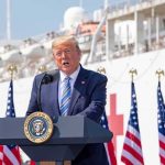 Language War Erupts At Mount Rushmore Donald Trump speaking at a podium with American flags and a ship in the background