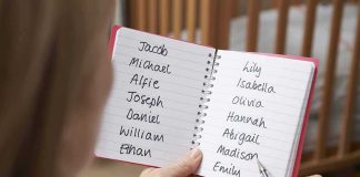 Hands holding a notebook with baby name lists near a crib