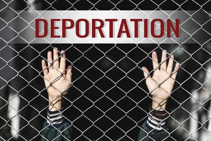 shutterstock_519187753 Hands gripping chain-link fence with deportation sign