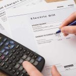 Schumer Cries Corruption Over Wind Deal hand reviewing utility bills with calculator on desk