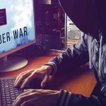 hooded person typing at a computer with multiple monitors