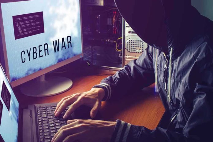 hooded person typing at a computer with multiple monitors