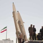 Iran Targets Big Tech — Missiles Ready Soldiers stand beside large missiles at an outdoor display