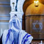 Synagogue Attack Erupts During Shabbat as Worshippers Scramble Person in white and blue prayer shawl facing ornate interior