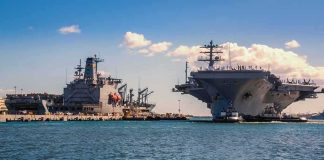 Top Admiral Says Iran Faces ‘DEVASTATING Costs’ Aircraft carrier and support ships docked at a naval harbor