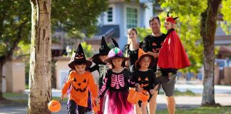 Children in Halloween costumes trick-or-treating with adults on a sunny street