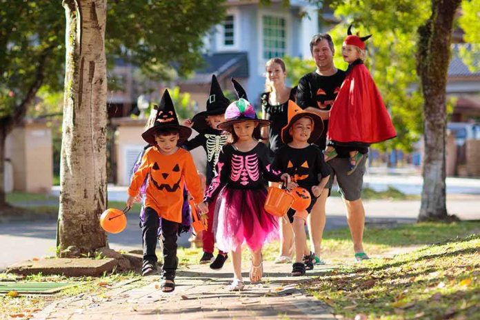 Children in Halloween costumes trick-or-treating with adults on a sunny street