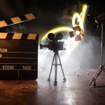 Hollywood Icon Dies At 102 Film clapperboard, vintage movie camera, and studio lights on a smoky set