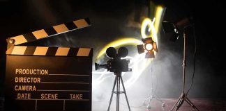 Hollywood Icon Dies At 102 Film clapperboard, vintage movie camera, and studio lights on a smoky set