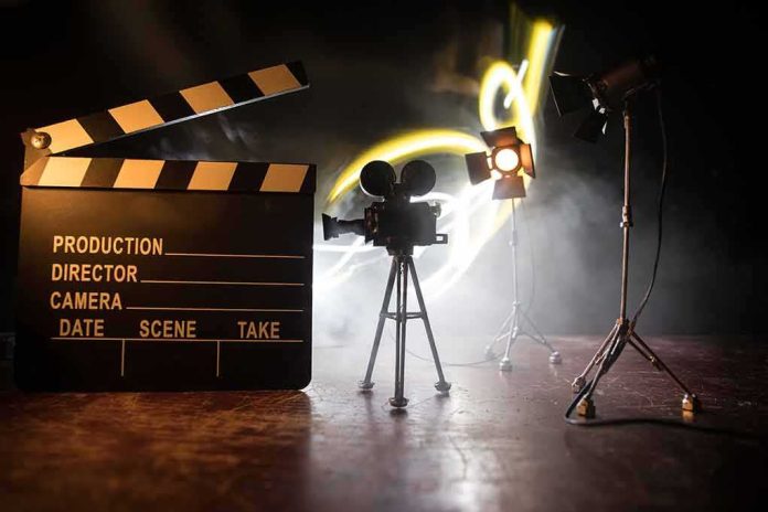 shutterstock_1727563630 Film clapperboard, vintage movie camera, and studio lights on a smoky set