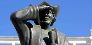 Bronze statue of a historical figure saluting against a blue sky
