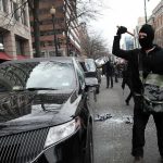 Masked protester raises tool to strike black car on city street